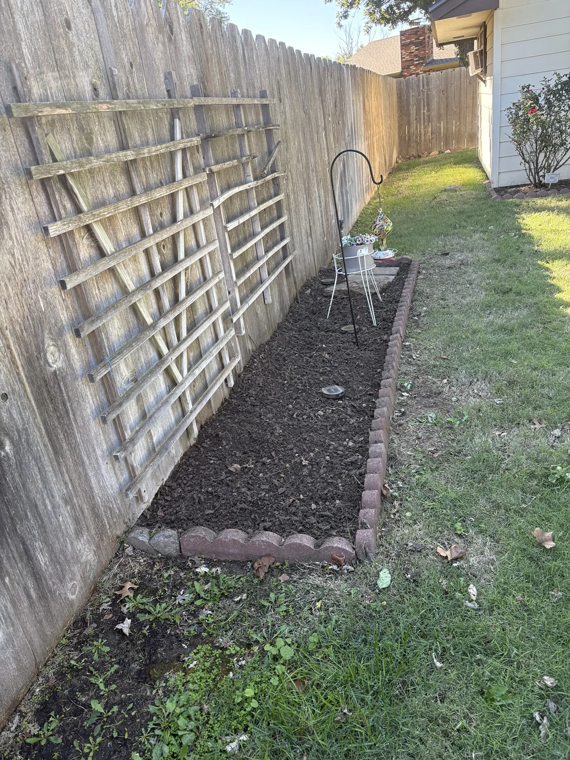 After: cleared flower bed with fresh dark mulch beside wooden fence